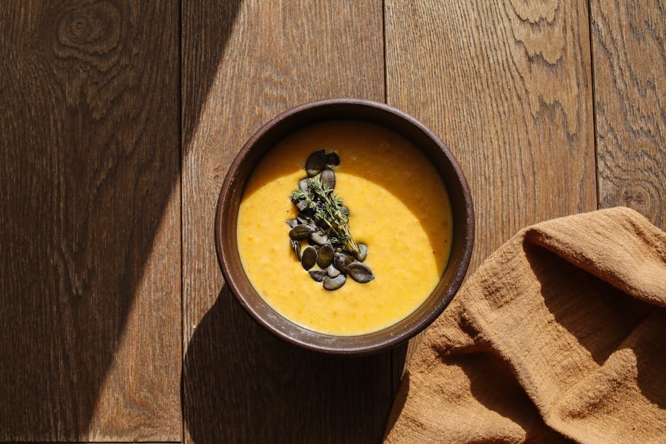 Warm pumpkin soup in a bowl with pumpkin seeds on a wooden table in natural light.