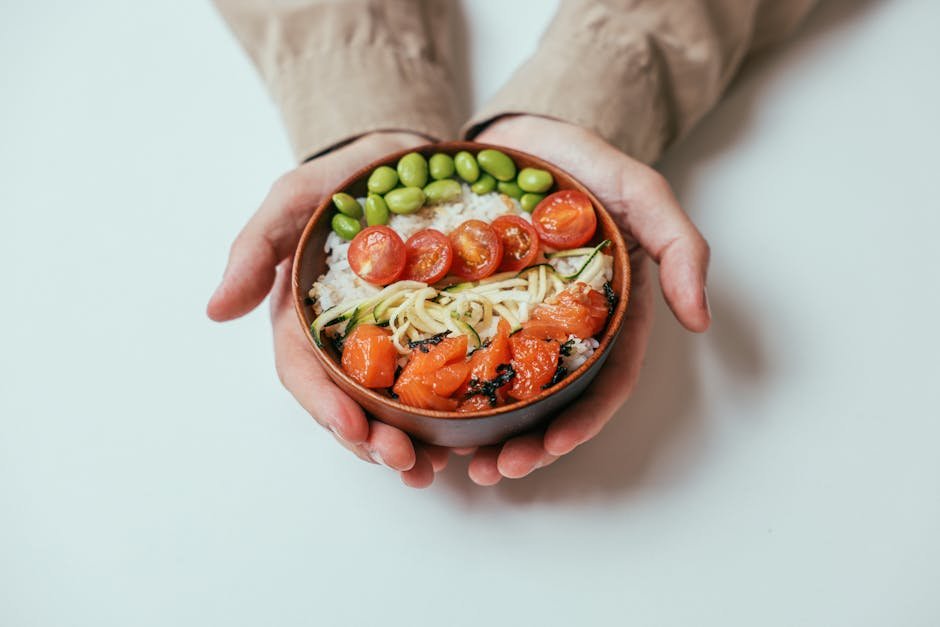 Close-up of hands holding a salmon poke bowl with cherry tomatoes, edamame, and rice.